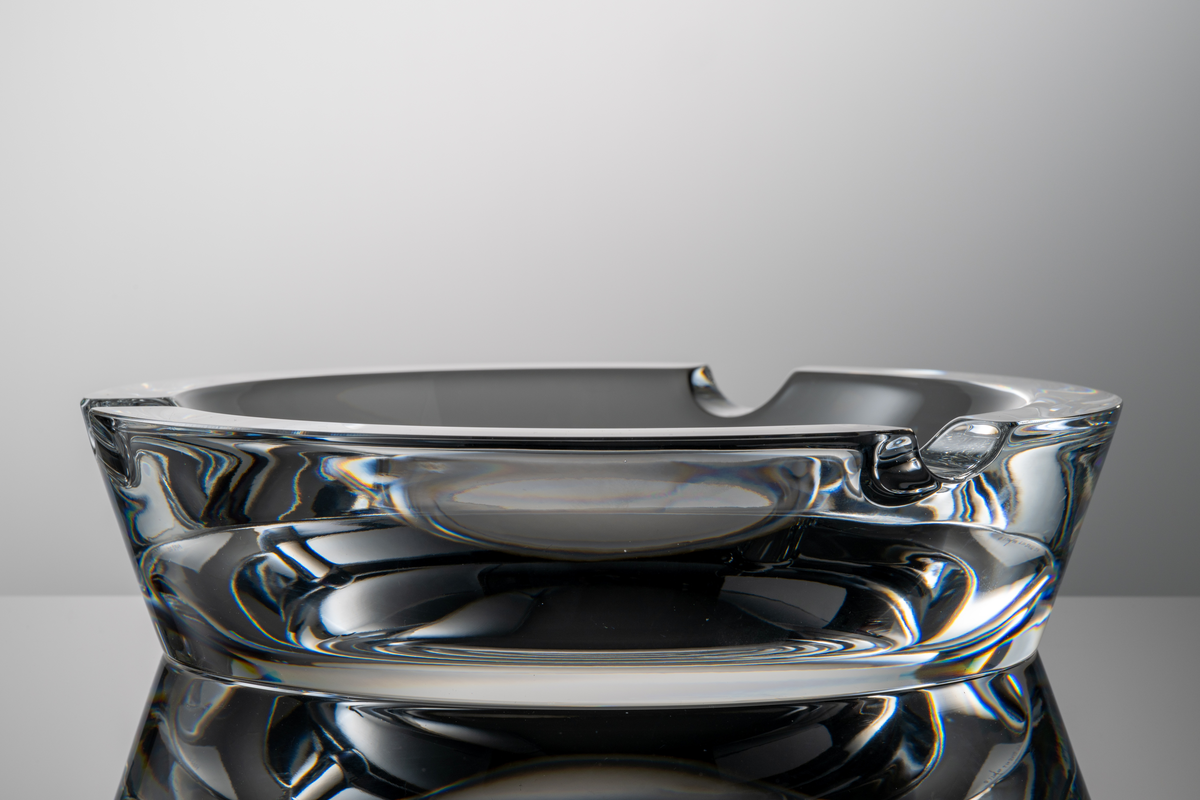 Formgivare: Lars Hellsten. Askfat i klarglas, rund form med tre urtag i mynningskanten.