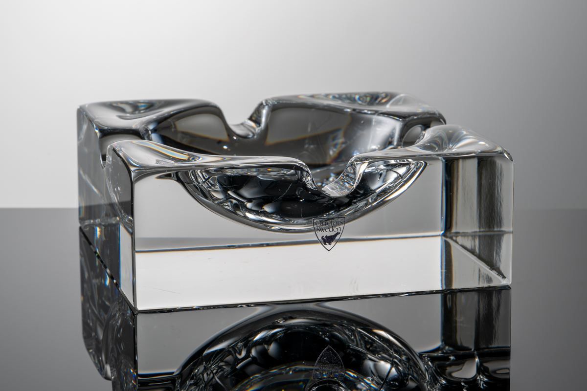 Formgivare: Lars Hellsten. Askfat i klarglas, kvadratisk form med fyra urtag i mynningskanten.