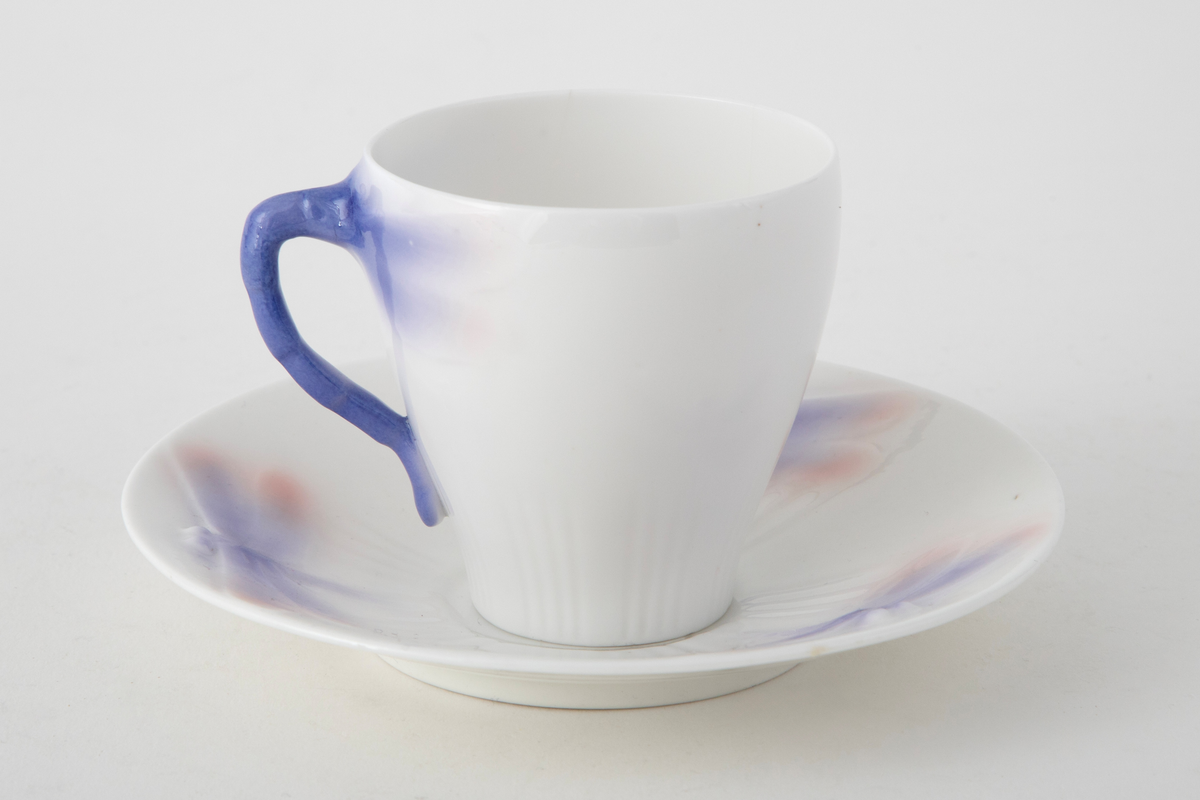 Sjablondreiet porselen. Hanken er støpt. Kopp med konisk form dekorert med plastiske øyenstikkere med rosa og blå underglasur på hvit grunn.
