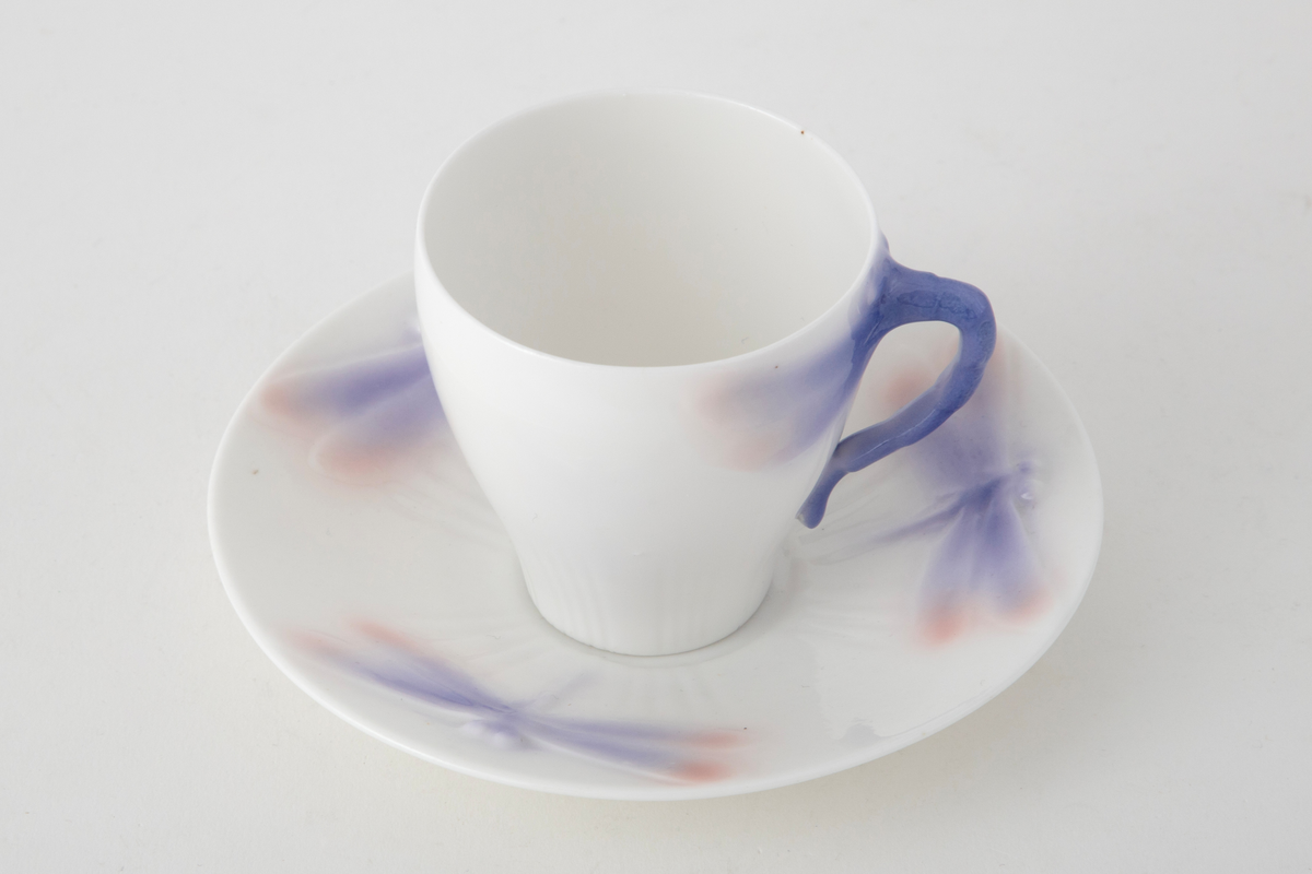 Sjablondreiet porselen. Hanken er støpt. Kopp med konisk form dekorert med plastiske øyenstikkere med rosa og blå underglasur på hvit grunn.