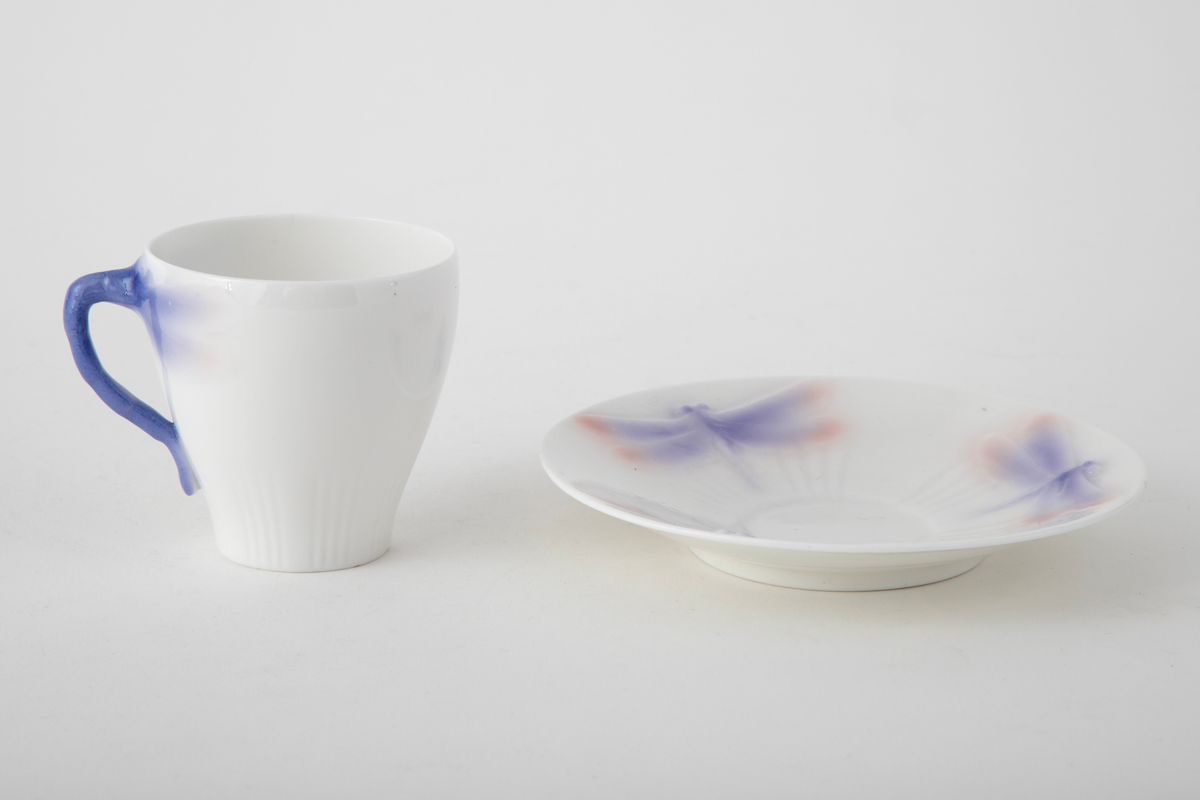 Sjablondreiet porselen. Hanken er støpt. Kopp med konisk form dekorert med plastiske øyenstikkere med rosa og blå underglasur på hvit grunn.