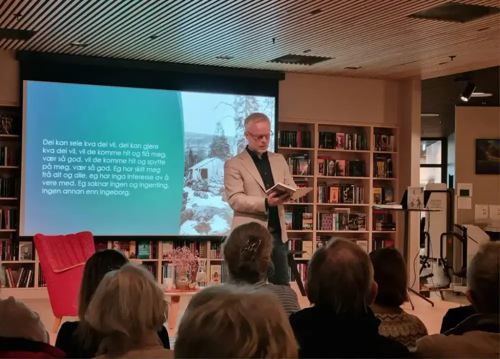 Bilete av Tore Renberg som les frå ei av bøkene sine på eit arrangement på Hareid folkebibliotek i regi av Litteraturhus i Møre og Romsdal. Publikum ser på.