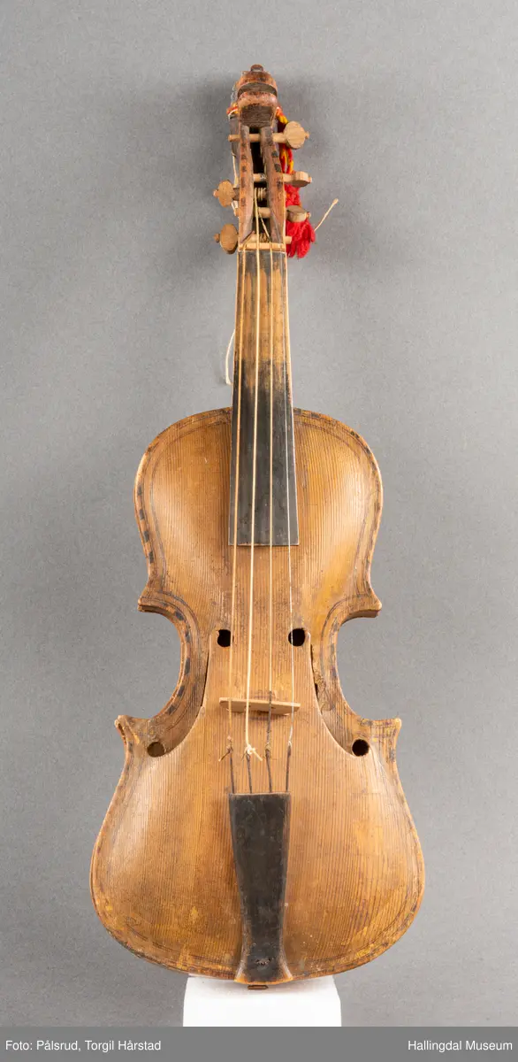 a) fele, b) bue, c) felekasse.  Bjerk, meget defekt resonanskasse.  Oversiden brukket i 3 løse deler.  Et stort stykke mangler.  Resonansbunnen lakkert, har malte profiler.  Har bare tre strenger.  Mangler flere nøkler.  Halsen avsluttes med utskåret løvehode.  Rød og gul ullsnor med dusk bundet fast til løvehodet.  Fingerbrettet har ingen gradering.  
b) Buen en rund pinne av gran.  I den ene enden skåret i L-form.  Feste for buestreng.  Strengen defekt.  I den andre enden er en takket jernbit festet i en snor.   Utsåret bjerkekloss festet i jerntråd.  
c) Gran, skåret.  Selve kassen består av et bredt bord, bøyd til hesteskoform og avsluttet med fire fjær til sinking i hver ende.  Sluttstykke mangler.  Bunnen laget av ett bord.  Festet til veggen med fire jernbeslag utvendig og en lærbit som erstatter et beslag.  Dette pluss ett av de andre beslagene går tvers over veggen og danner hengsler for lokket som er laget av ett bord, svakt hvelvet.   Liten k jernkrampe i lokk-kanten.  Tilsvarende i veggen.  Beslaget  på toppen av "hesteskoen" har en liten jernkrampe med jernring.  Lokk og vegger er overmalt.  Bunnfarge brun.  Veggen akantus i gult, sort , blått og hvitt.  Beslagene blåmalt.  På samme side som jernkrampe bokstaver og tall malt med gult:  KITTIL HARALSSEN 1843.  Veggen har to store hull.  Lokket har blomsterdekor i samme farge som veggene.  Innvendig brunmalt.  Stort stykke spikket bort.  18/8-64. Å Astrup

Fela er nå restaurert og satt i full stand. 5/3-1979, K.K.Nøklebye