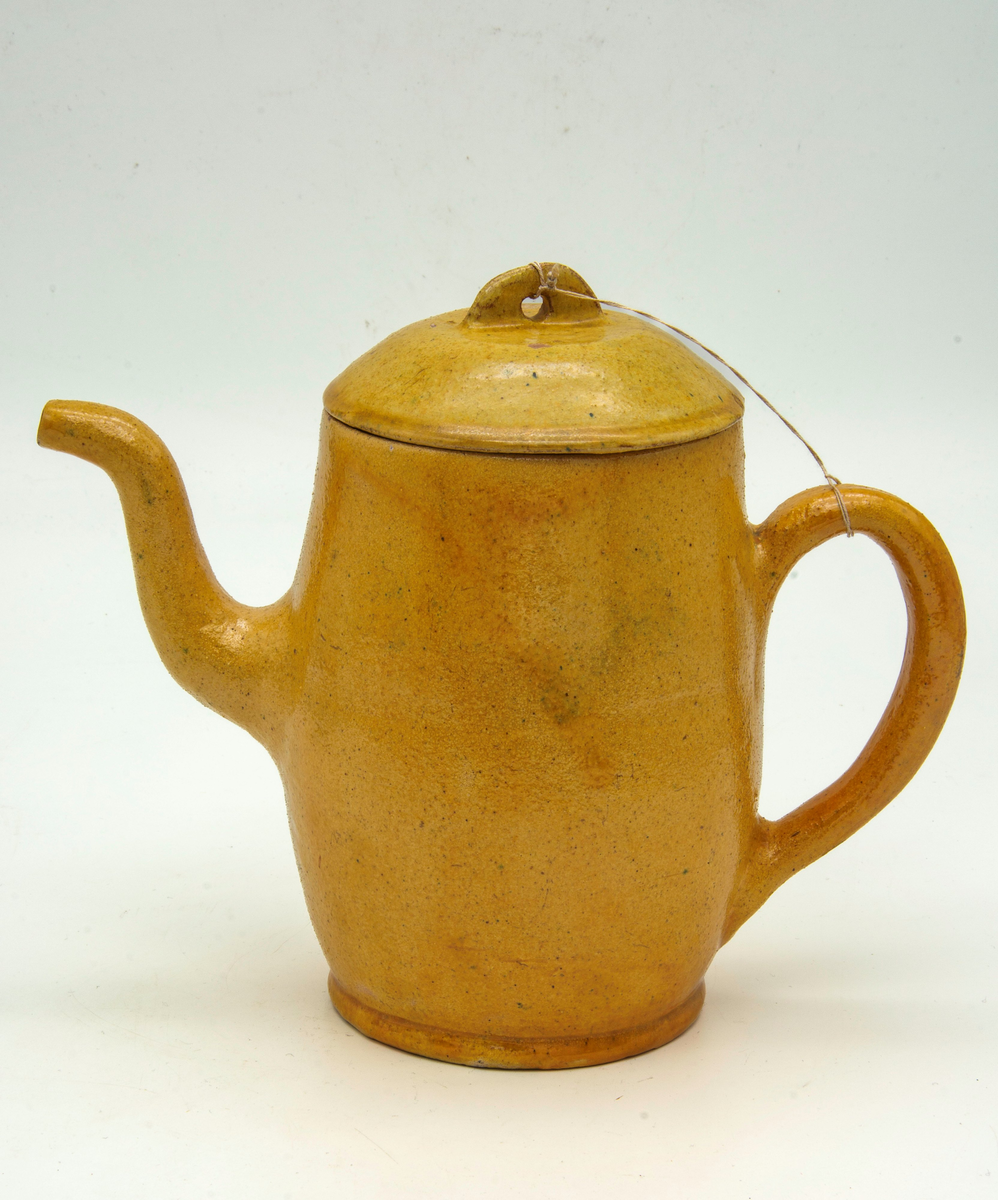 Tekanna av lergods. a) Kanna, handdrejad, gul, glaserad. Handtag i sidan, pip. På undersidan inristat: "Aug. Cederholm Warberg". b) Lock, handdrejat, gult, fals, glaserat. Tumgrepp med hål. Höjd, (inklusive tumgrepp), 4 cm. Övre diameter:100 mm. Nedre diameter:100 mm. 