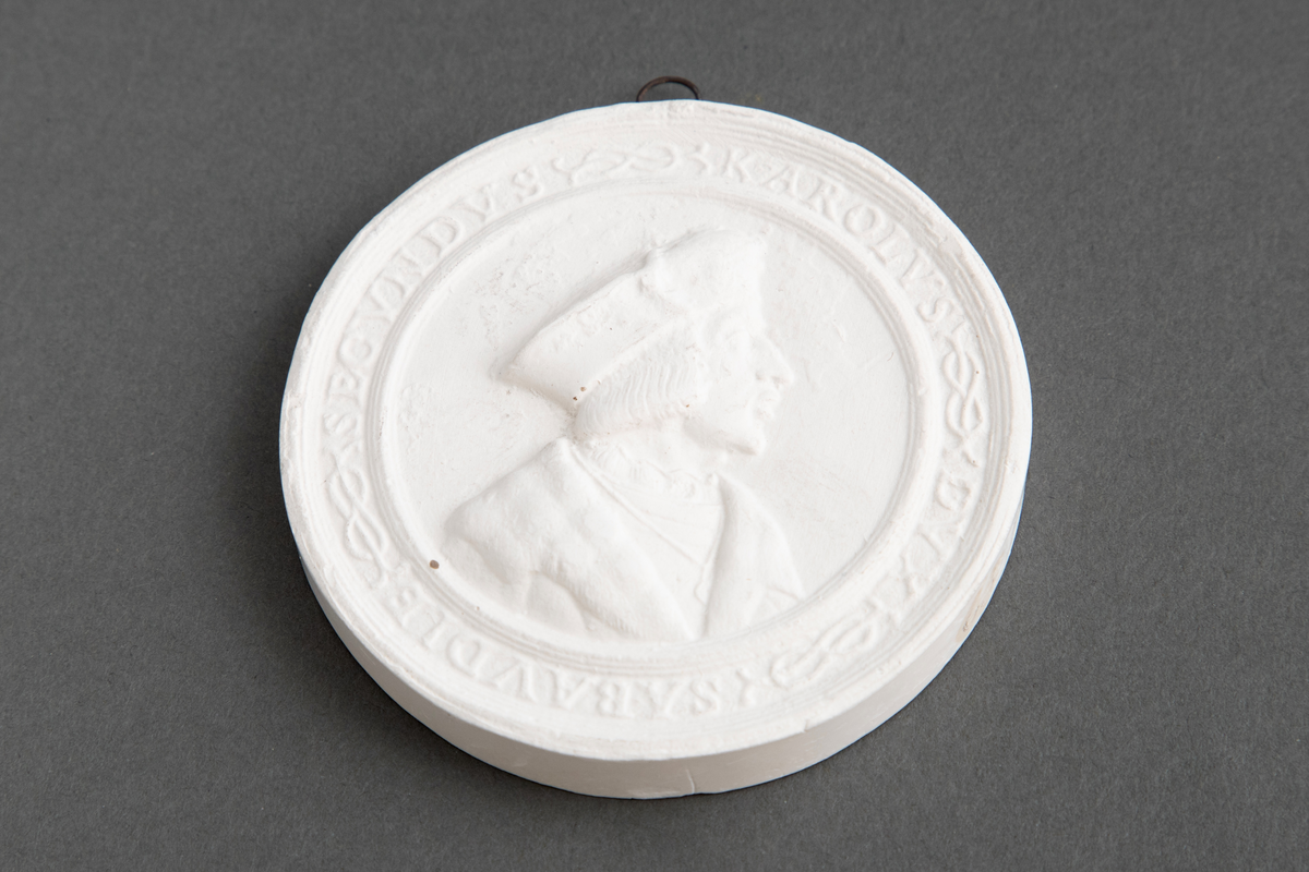 Avstøpning av bronseplakett. Hempe i metall for opphenging.