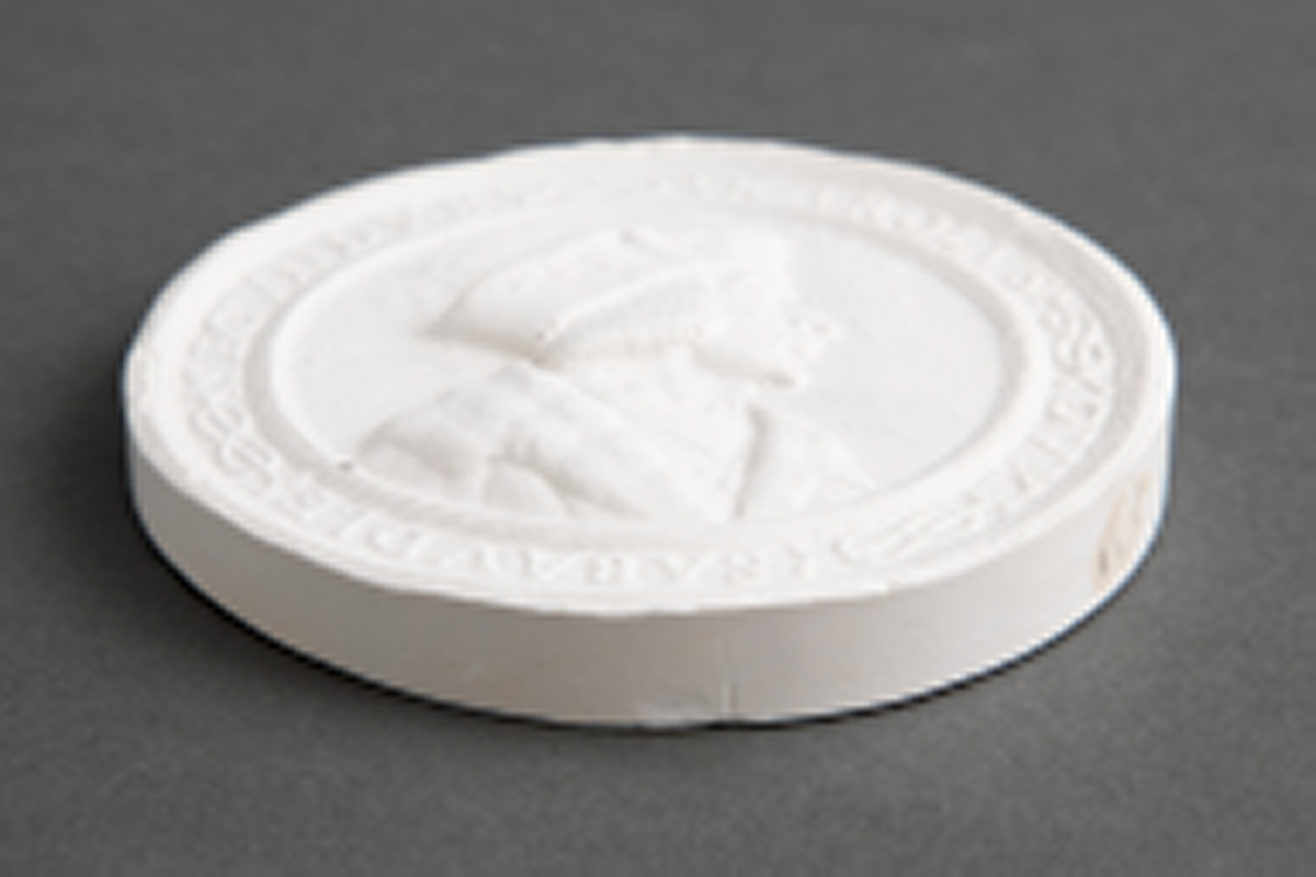 Avstøpning av bronseplakett. Hempe i metall for opphenging.