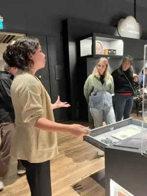 En kvinna har visning för andra personer i en utställning med montrar i bakgrunden.