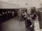Kalmar Telefonstation omkr. år 1930. Personal vid växelbord. Ltf Gunhild Svensson, eltf Elsa Kaarlsson, lntf Berta Ljunggren, ltf Elisabet Blomqvist, lts Agda Nordberg, eltf Ingrid Hultenius, Tk A.G. Johansson, vf Alba Strandberg, ertf Anna Eiding, intf Mimmi Ardén, lntf Nina Lisa Johansson, ertf Elsa Johnsson, rtf Rut Rundqvist, rtf Helfrid Niklasson och lntf Greta Andersson.