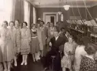Skara Telefonstation omkr. år 1930. Telefonsal. Gruppfoto. Ltf Märta Berg, lntf Elly Lindkvist, eltf greta Andersson, ltf Gertrud Nilsson, eltf Annalisa Nyqvist, ltf Anna Nyström, ltf Hulda Svensson, ltf Gerd Cederborg, rtf Elsa Bäckström, lntf Alli Frisell, rtf Märta Tyrén, eortf Maja Hällström, rtf Maja Svanbom, tk Alfred Falck, ltf Vesta Bergman, lntf Ella Djerf, rtf Anna Johansson.