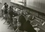 Stockholms riksstation 1950-talet, NK-längan U49 i R 10-11. Längan var normal men kompletterad med en överbyggnad (s.k. lostet) med lampor i knappar för 100 ledn, per exp.plats. Telefonisten fällde en EO-omk. I en insats i bordskivan och tryckte på någon av knapparna i 