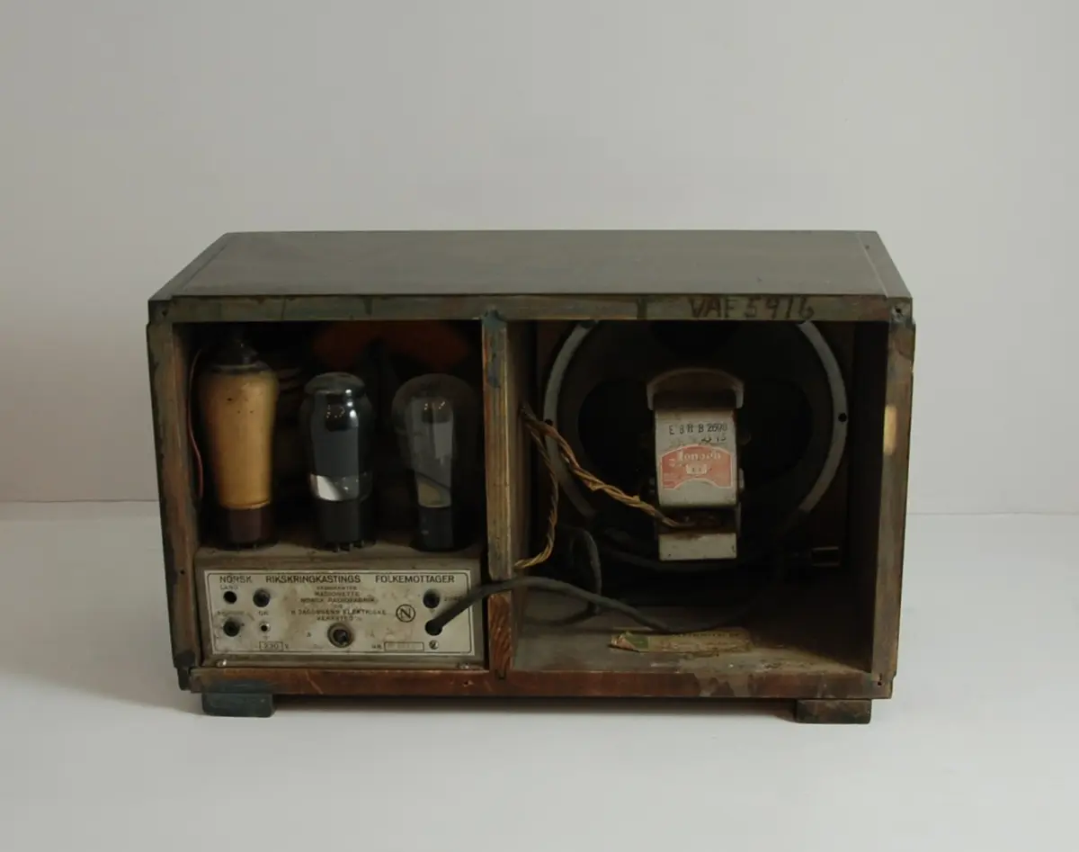 Radio, bordmodell. Rektangulær trekasse av beiset bøk med falset topp og sideplater, samt to lave, rektangulære lister til ben. Fremsiden har et sirkulært hull til høyttaler dekket av en champagnefarget stoff. Stasjonssøkeren har buesegmentformet innramming i sort bakelitt med tre brune bakelittknotter under for tilkobling, av og på, søker og volum. I søkerskivens venstre del står produsentinformasjon. Søkerskiven har lang og mellombølge.