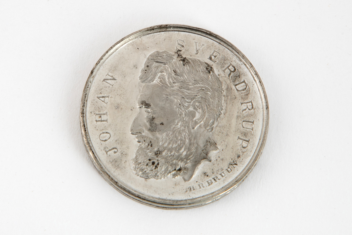 Rund medalje med mannsportett på avers side og laurbærgrener på revers side. Begge sider har omskrift.