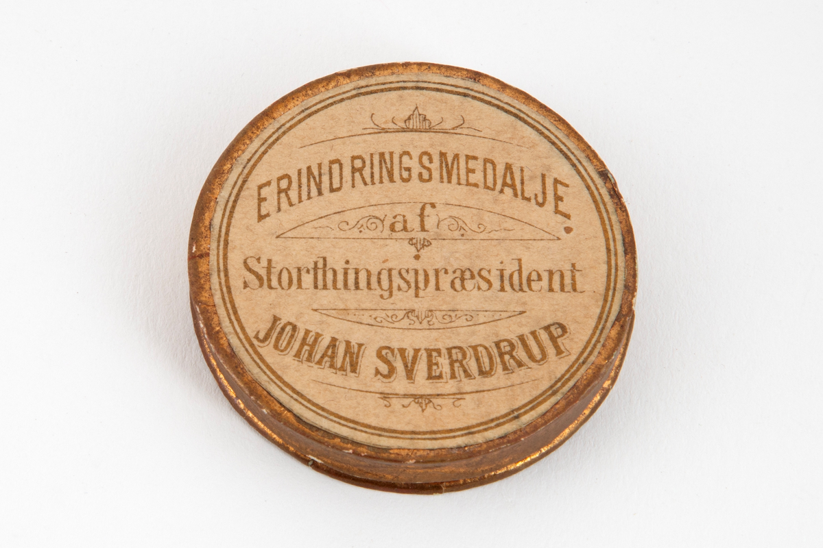 Rund medalje med mannsportett på avers side og laurbærgrener på revers side. Begge sider har omskrift.