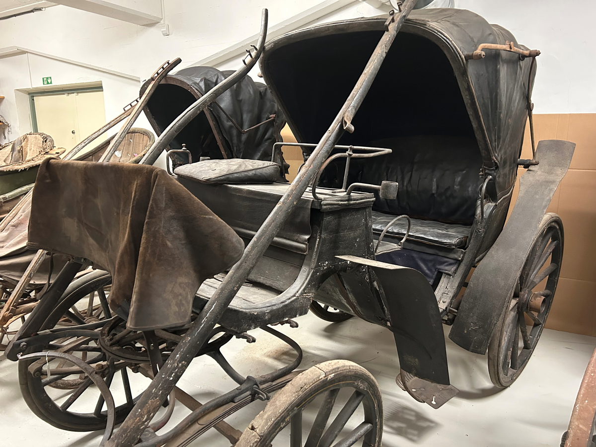 Svartmålad. Fyrhjulig hästvagn. Vagnen har öppen kuskbock med möjlighet att dra sufflett över passagerarplatsen. Huvudsäte för framåtresande men litet klätt nedfällbart säte för bakåtresande. Sätena är klädda med svart skinn. Fotsteg på varje sida.  Två skaklar framtill. Stänkskydd monterade på bakhjulen. Bakhjulen större än framhjulen.