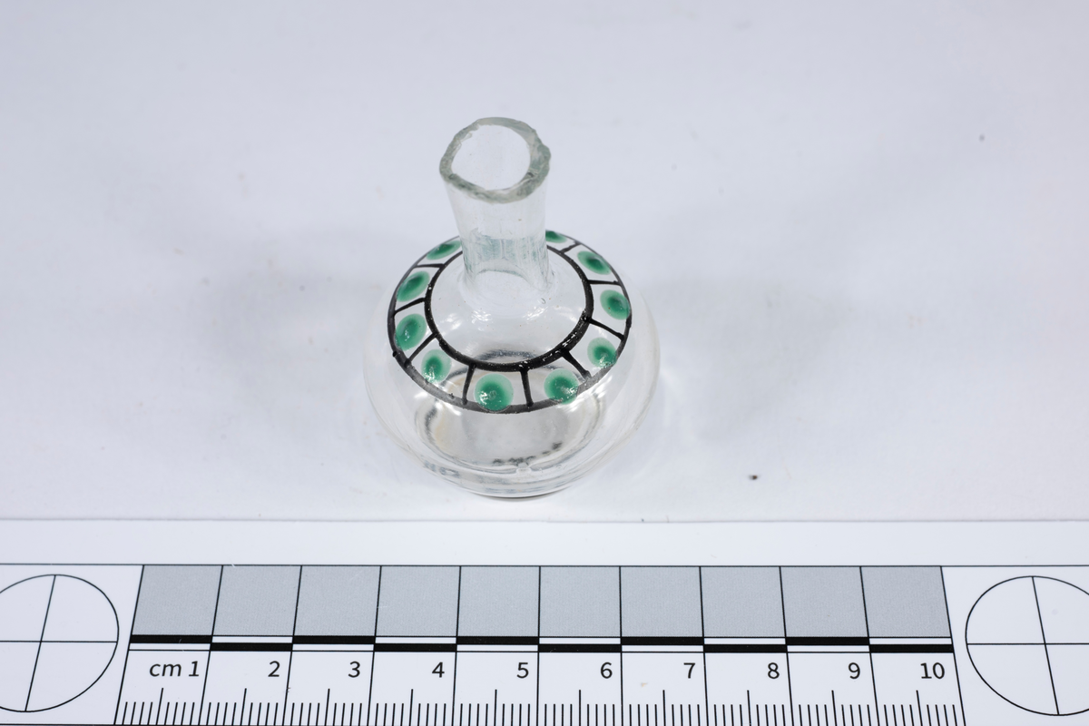 Föremålet består av fotplatta, sfärisk buk och smal hals med vidgad mynning. Dekoration: svartmålad ring runt hela fotplattan, två svartmålade parallella streck med vertikala streck som delar utrymme mellan cirklarna i elva delar, i varje del finns en grön prick.