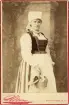 Operasångerskan Christina Nilsson i Vingåkersdräkt.
Knäbild, halvprofil. Ateljéfoto. 
Under fotot text: 