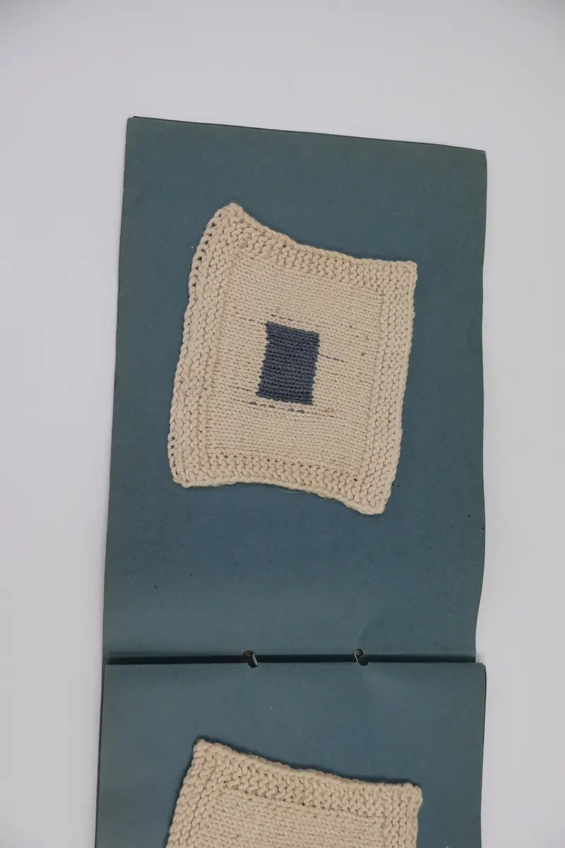 Provbok med stoppsömmar. Egenhändigt tillverkad bok av vikta ark i gråblå kartong sammanfogade med ett slitet rosa sidenband knutet i rosett. Handskriven text i vitt på framsidan: "STOPPNING  IRMA WELIN.".
- På första uppslaget, höger sida står det: "Rutstopp."
Stoppsömmen är sydd med rött ullgarn i form av en kvadrat mitt på den 120 x120 mm stora bottenväven i panamabindning. Fållad med sicksack-bård innanför fransen.
- Nästa uppslag visar prov på två två olika maskstoppar på var sin slätstickad lapp med rätstickad kant längs alla fyra sidor. Lapparna är stickade i oblekt bomullsgarn, maskstopparna i blågrått bomullsgarn i form av en kvadrat mitt på lappen. På den högra sidan står överst: "Äkta maskstopp.".
- Tredje uppslaget, till vänster ytterligare en stickad lapp i oblekt bomullsgarn. Resårstickad med rätstickad kant runt om. Maskstopp i blågrått bomullsgarn i en kvadratisk ruta mitt på lappen.
På höger sida står det med vit text: "Mönsterstopp till gåsögon.". En gles klistrad väv i vitt med mönsterstoppning i rött garn i den ena riktningen och blått garn i den andra riktningen i form av ett gåsöga. Röd broderad bård innanför fransen.
- Fjärde uppslaget, till höger; ett prov på beige gabardintyg, mönsterstoppat/konststoppat på två ställen med tråd i samma färg. Text högst upp: "Mönsterstopp-till-gabardin.".
- Nästa uppslag, till höger visar ett rutigt kostym-/dräkttyg vävt i kypert med prov på en fin lagning. Överst står det: "Lagning-av-revor.".
- Sista uppslaget, till höger visar två prover på tyllstoppning. En kvadratisk kartongbit 70 x 70 mm med två nyanser rött garn trätt upp och ned igenom kartongen till ett nät. Trädning/stopp med blått garn över halva ytan. Intill sitter en bit vit tyll med en lagning/stopp mitt på. Text överst på sidan: "Tyllstopp.".