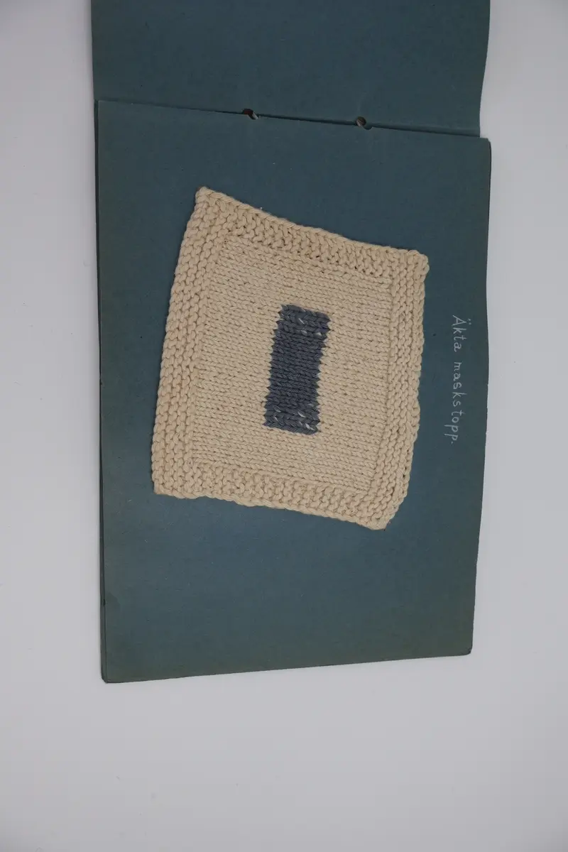 Provbok med stoppsömmar. Egenhändigt tillverkad bok av vikta ark i gråblå kartong sammanfogade med ett slitet rosa sidenband knutet i rosett. Handskriven text i vitt på framsidan: "STOPPNING  IRMA WELIN.".
- På första uppslaget, höger sida står det: "Rutstopp."
Stoppsömmen är sydd med rött ullgarn i form av en kvadrat mitt på den 120 x120 mm stora bottenväven i panamabindning. Fållad med sicksack-bård innanför fransen.
- Nästa uppslag visar prov på två två olika maskstoppar på var sin slätstickad lapp med rätstickad kant längs alla fyra sidor. Lapparna är stickade i oblekt bomullsgarn, maskstopparna i blågrått bomullsgarn i form av en kvadrat mitt på lappen. På den högra sidan står överst: "Äkta maskstopp.".
- Tredje uppslaget, till vänster ytterligare en stickad lapp i oblekt bomullsgarn. Resårstickad med rätstickad kant runt om. Maskstopp i blågrått bomullsgarn i en kvadratisk ruta mitt på lappen.
På höger sida står det med vit text: "Mönsterstopp till gåsögon.". En gles klistrad väv i vitt med mönsterstoppning i rött garn i den ena riktningen och blått garn i den andra riktningen i form av ett gåsöga. Röd broderad bård innanför fransen.
- Fjärde uppslaget, till höger; ett prov på beige gabardintyg, mönsterstoppat/konststoppat på två ställen med tråd i samma färg. Text högst upp: "Mönsterstopp-till-gabardin.".
- Nästa uppslag, till höger visar ett rutigt kostym-/dräkttyg vävt i kypert med prov på en fin lagning. Överst står det: "Lagning-av-revor.".
- Sista uppslaget, till höger visar två prover på tyllstoppning. En kvadratisk kartongbit 70 x 70 mm med två nyanser rött garn trätt upp och ned igenom kartongen till ett nät. Trädning/stopp med blått garn över halva ytan. Intill sitter en bit vit tyll med en lagning/stopp mitt på. Text överst på sidan: "Tyllstopp.".