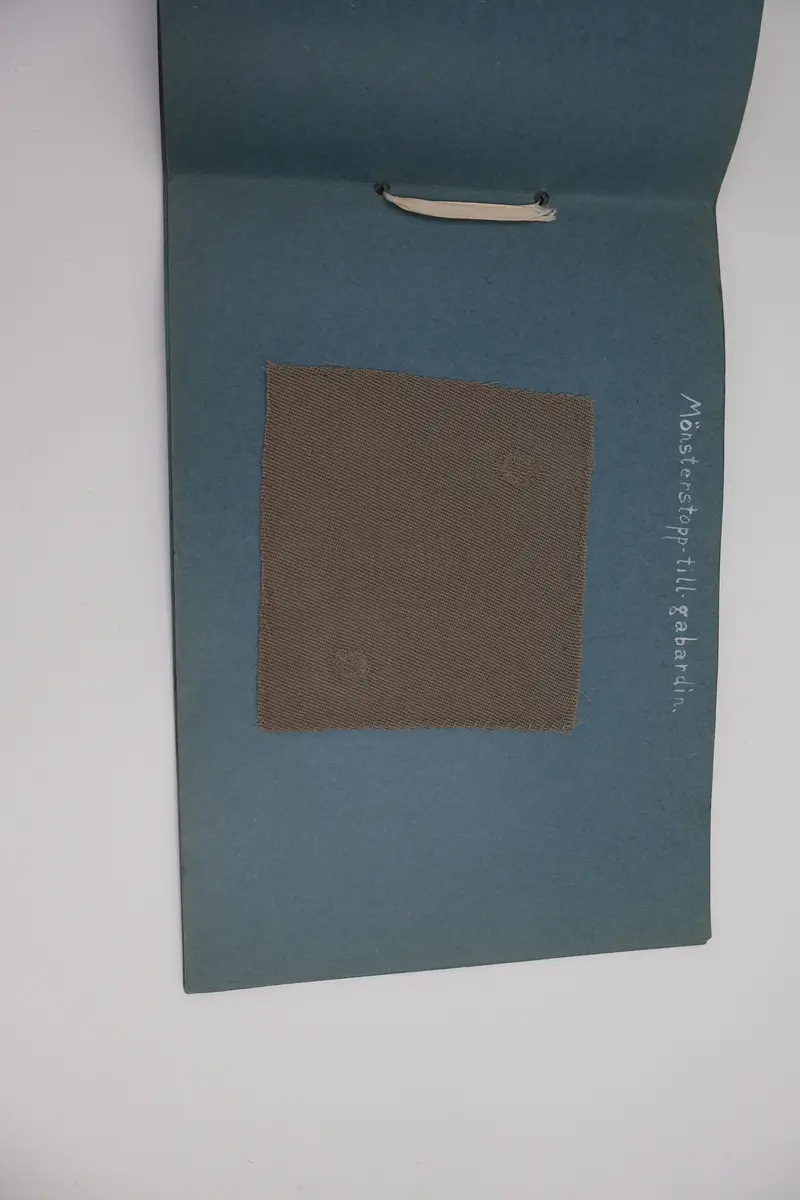 Provbok med stoppsömmar. Egenhändigt tillverkad bok av vikta ark i gråblå kartong sammanfogade med ett slitet rosa sidenband knutet i rosett. Handskriven text i vitt på framsidan: "STOPPNING  IRMA WELIN.".
- På första uppslaget, höger sida står det: "Rutstopp."
Stoppsömmen är sydd med rött ullgarn i form av en kvadrat mitt på den 120 x120 mm stora bottenväven i panamabindning. Fållad med sicksack-bård innanför fransen.
- Nästa uppslag visar prov på två två olika maskstoppar på var sin slätstickad lapp med rätstickad kant längs alla fyra sidor. Lapparna är stickade i oblekt bomullsgarn, maskstopparna i blågrått bomullsgarn i form av en kvadrat mitt på lappen. På den högra sidan står överst: "Äkta maskstopp.".
- Tredje uppslaget, till vänster ytterligare en stickad lapp i oblekt bomullsgarn. Resårstickad med rätstickad kant runt om. Maskstopp i blågrått bomullsgarn i en kvadratisk ruta mitt på lappen.
På höger sida står det med vit text: "Mönsterstopp till gåsögon.". En gles klistrad väv i vitt med mönsterstoppning i rött garn i den ena riktningen och blått garn i den andra riktningen i form av ett gåsöga. Röd broderad bård innanför fransen.
- Fjärde uppslaget, till höger; ett prov på beige gabardintyg, mönsterstoppat/konststoppat på två ställen med tråd i samma färg. Text högst upp: "Mönsterstopp-till-gabardin.".
- Nästa uppslag, till höger visar ett rutigt kostym-/dräkttyg vävt i kypert med prov på en fin lagning. Överst står det: "Lagning-av-revor.".
- Sista uppslaget, till höger visar två prover på tyllstoppning. En kvadratisk kartongbit 70 x 70 mm med två nyanser rött garn trätt upp och ned igenom kartongen till ett nät. Trädning/stopp med blått garn över halva ytan. Intill sitter en bit vit tyll med en lagning/stopp mitt på. Text överst på sidan: "Tyllstopp.".