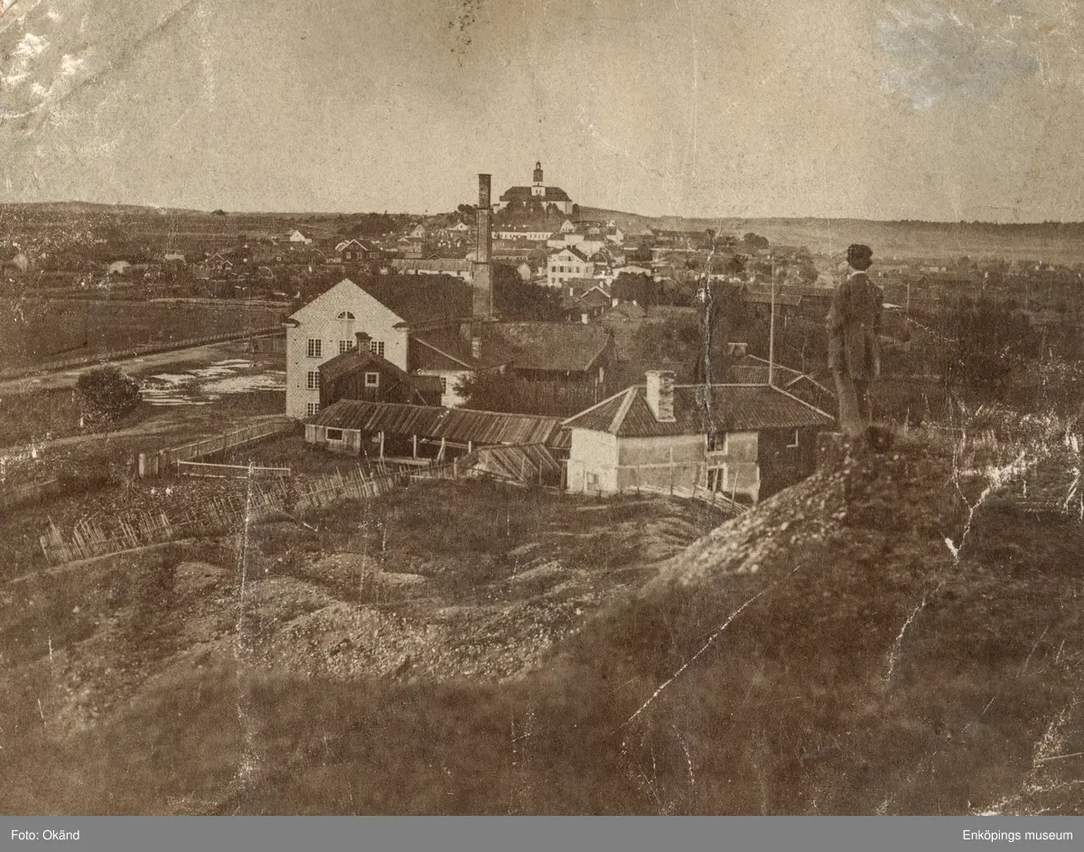 Vy över staden i början av 1860-talet, bilden är tagen från Gröngarnsåsen vid Lustigkulla. Trähuset i förgrunden till vänster är det fattighus som revs 1883. Huset bakom med den höga skorstenen är bränneriet. Framför kyrkan ses Långholmen och rådhuset och framför rådhuset Lagerströmskahuset vid torget.

Ett av de äldsta fotografierna över Enköping. Fotograf: Okänd