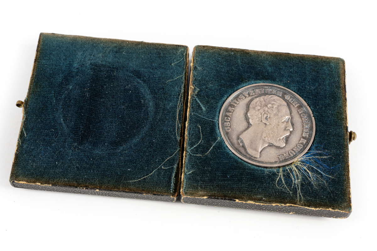 Medalj av silver utdelad av Kalmar läns hushållningssällskap, sannolikt som pris eller belöning för arbete, skicklighet eller prestation inom lantbruk eller liknande.