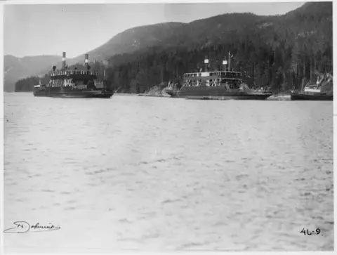 D/F Ammonia er sjøsatt etter å ha ligget på slippen på Tinnoset. Flagg henger fra baugen og opp i flaggstanga. Mennesker stående på baugen. D/F Hydro ligger i vannet ved siden av og D/S Gausta foran.