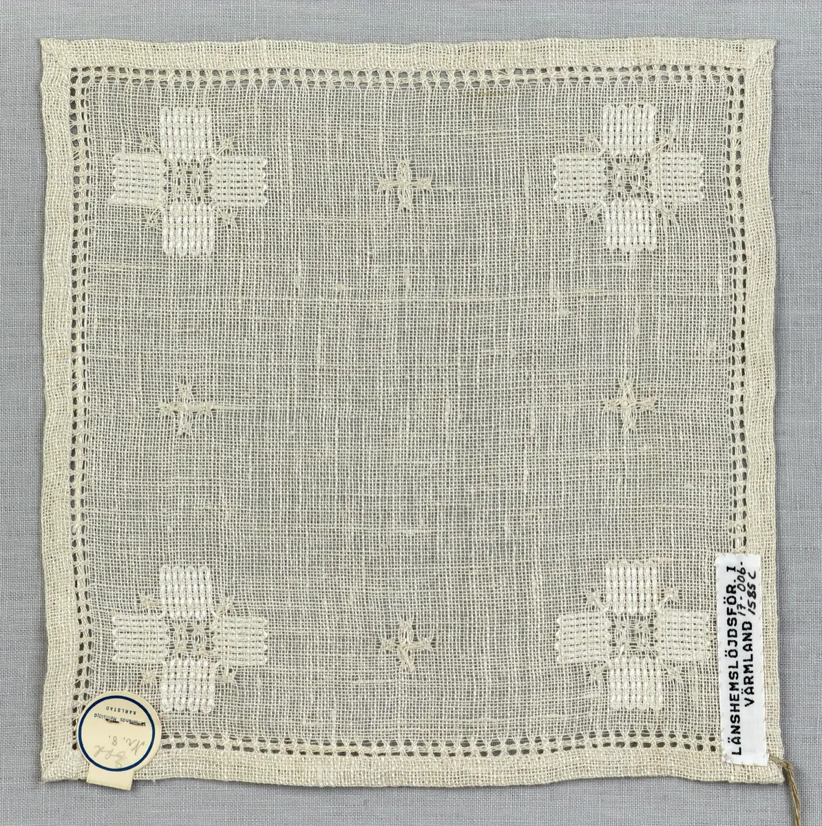 Duk gjord av linneväv med 8tr/cm i tuskaft och broderi utfört med merceriserat bomullsgarn i stoppstygn samt knyppeltråd i slingerstygn och myrgång sydd över fyra trådar. Duken har 9mm bred dubbelvikt fåll runt om och sneda hörn fastsydda med kaststygn.
