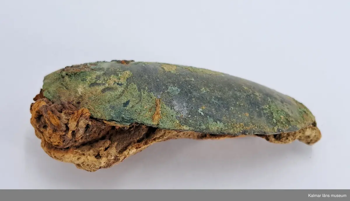 KLM 46818:3359. Spännbuckla. Helt slät och oornerad spännbuckla av brons. Med textilfragment som sitter kvar på undersidan.