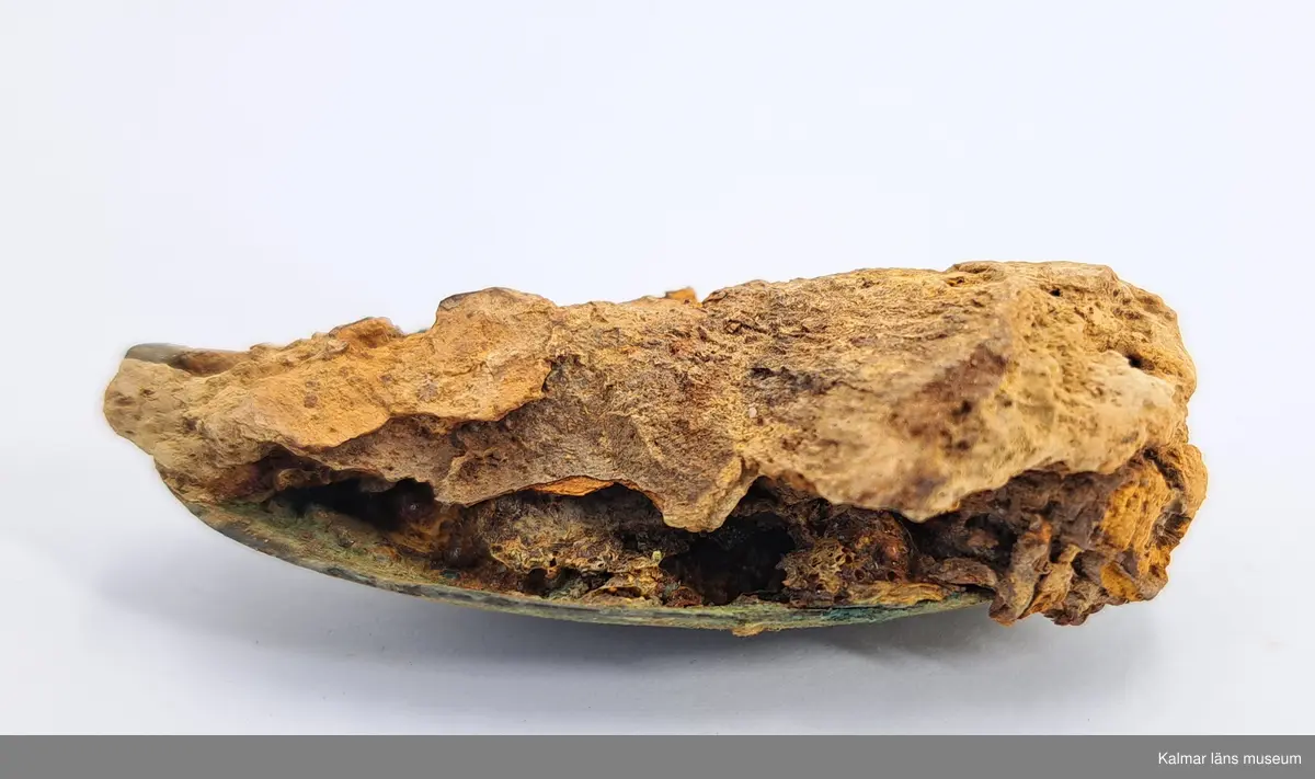 KLM 46818:3359. Spännbuckla. Helt slät och oornerad spännbuckla av brons. Med textilfragment som sitter kvar på undersidan.