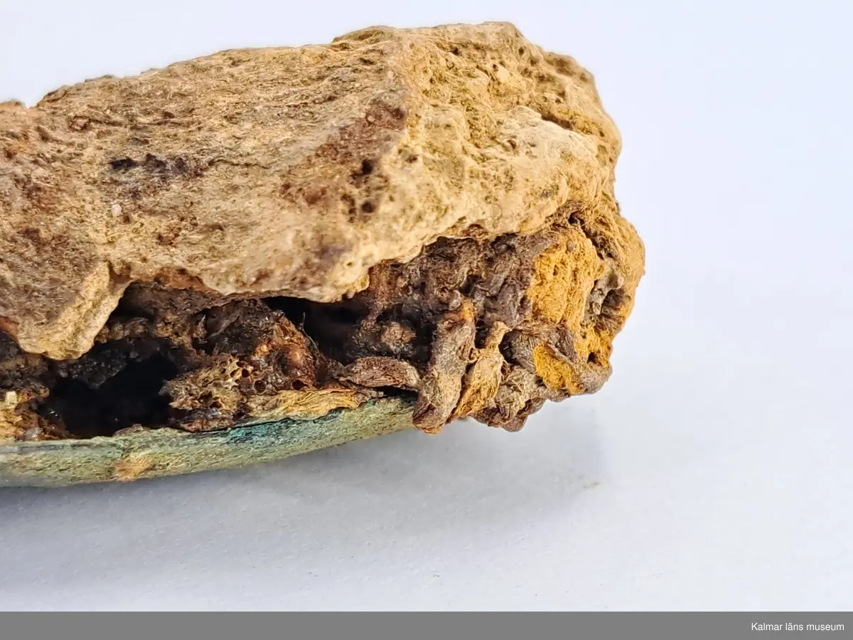 KLM 46818:3359. Spännbuckla. Helt slät och oornerad spännbuckla av brons. Med textilfragment som sitter kvar på undersidan.