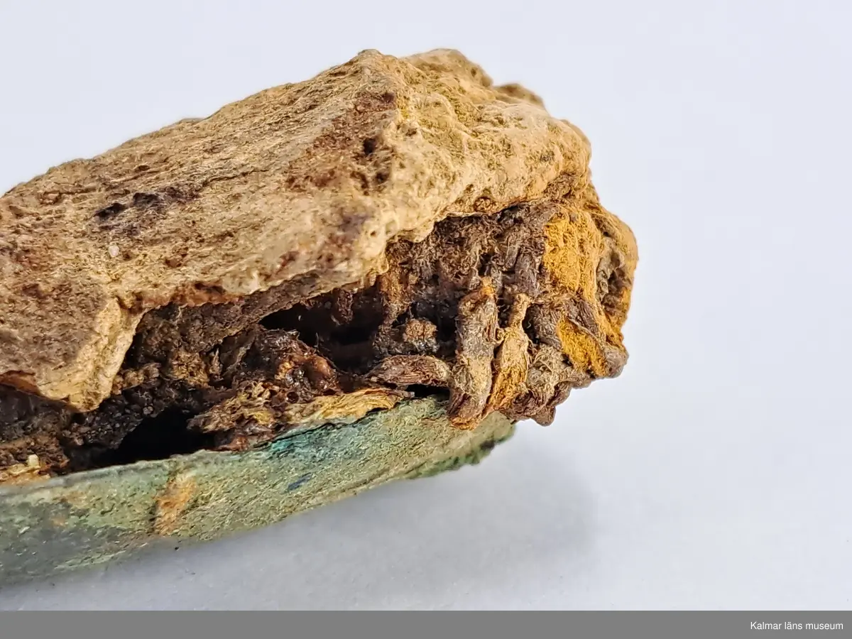 KLM 46818:3359. Spännbuckla. Helt slät och oornerad spännbuckla av brons. Med textilfragment som sitter kvar på undersidan.