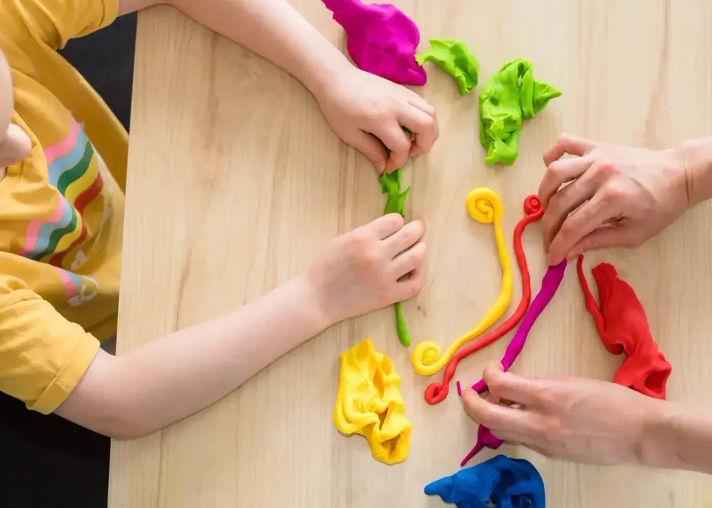 Två par barnhänder pysslar med lera i olika färger.