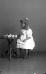 Porträtt av okänd liten flicka sittande vid en barnmöbel med kaffekoppar på bordet.
