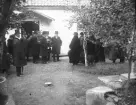 Ett begravningsfölje vid en liten stuga.