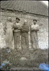 Fire menn i arbeidsklede foran ei bygning av murstein.