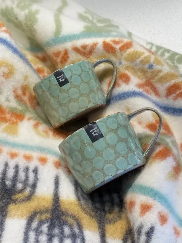 Gröna keramikmuggar med prickar och en mönstrad ullpläd