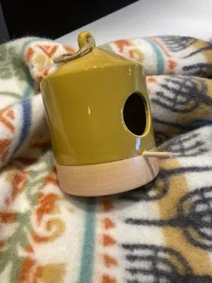 En gul fågelmatare i keramik står på en mönstrad ullpläd