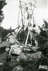 Flere unge menn bygger et tårn av stokker. I bakgrunnen skim