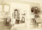 Rumsinteriör. Sannolikt från Galoschbolagets hus i Gävle, sent 1800-tal. Fotografierna uppe till höger i bild föreställer Josefina Albertina Mattsson f. Larsson samt Hans Anders Mattsson (enligt text till bilderna i album).