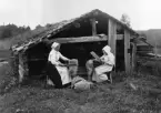 Linskäktning, två kvinnor arbetar framför en timrad byggnad. Åkerö, Leksands socken i Dalarna.