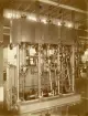 En trecylindrig kompoudångmaskin står på fabriksgolvet i F. Schishaus maskinmonteringshall, där den är tillverkad. Maskinen är konstruerad av ingenjören Carl H. Zuese i Elbing år 1881 och är den första av sitt slag att konstrueras och byggdas på den europeiska kontinenten.