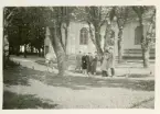 Ett sällskap som står framför en byggnad, troligen i stadsmiljö. Tryckt namn i nedre högra hörnet: Arvid Posse, troligen fotografens.