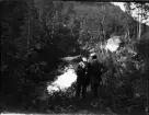 Två män står och tittar ner på forsande vatten, Uppland