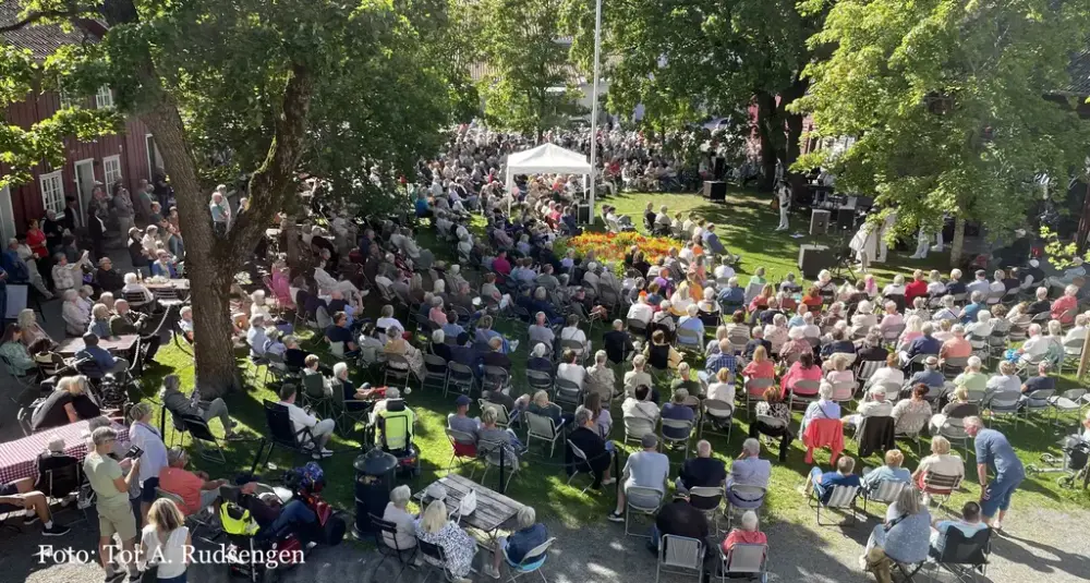 Tunet på Gjøvik gård sett ovenfra, fullt av mennesker sitter på en grønn plen og ser på noen som holder en konsert. 