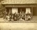 Gruppbild av Vegaexpeditionens medlemmar framför Sumaderatemplet i Kobe, Japan, där de bjudits på fest. De poserar med öppnade vinflaskor och fyllda glas.