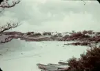 En sandstrand på Bermuda omgiven av klippor. I bakgrunden ligger hus och i förgrunden är tre små båtar uppdragna på stranden. Människor badar i vattnet.
