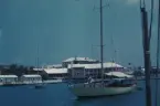 Royal Bermuda Yacht Clubs klubbhus fotograferat från vattnet i Hamilton Harbour. I förgrunden ligger två segelbåtar ankrade.