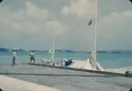 Knud H. Reimers yawl Hazard III ligger förtöjd vid en kaj i St. George's Harbour, Bermuda. Seglen är utspridda över däck för att torka efter deltagandet i Newport Bermuda Race 1954. Mannen på HAZARD IIIs däck skulle kunna vara Reimers.