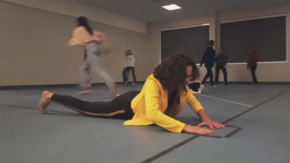 ei jente ligg på eit golv i gymsalen med fleire born i bakgrunnen