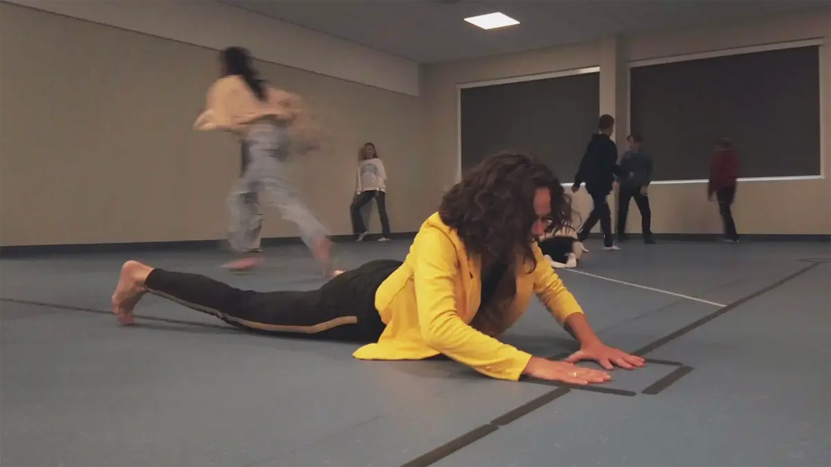 ei jente ligg på eit golv i gymsalen med fleire born i bakgrunnen